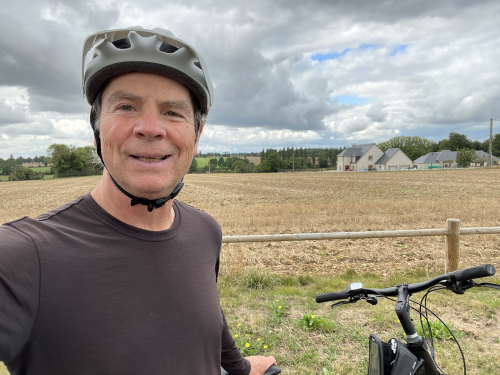 Jim Williams on bike with helmet in front of a field