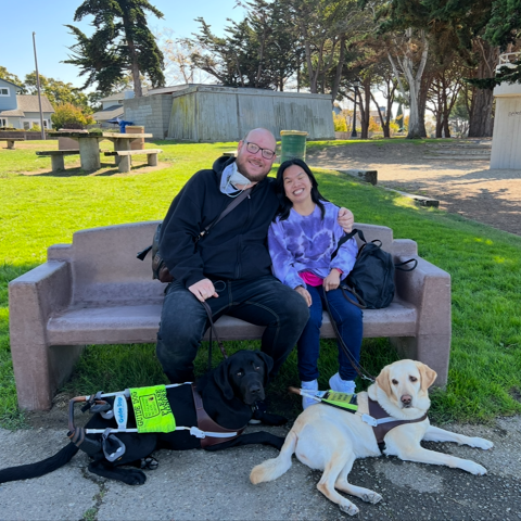 Erik and Michaela smiling on park bench with two guide Labradors