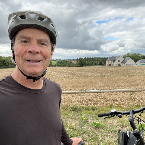 Jim Williams on bike with helmet in front of a field