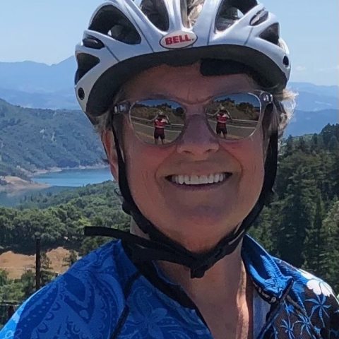 Woman with bike helmet and reflective sunglasses, with mountains in background  